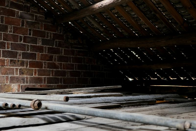 Dusty roof space with timber framing, floorboards and a brick wall
