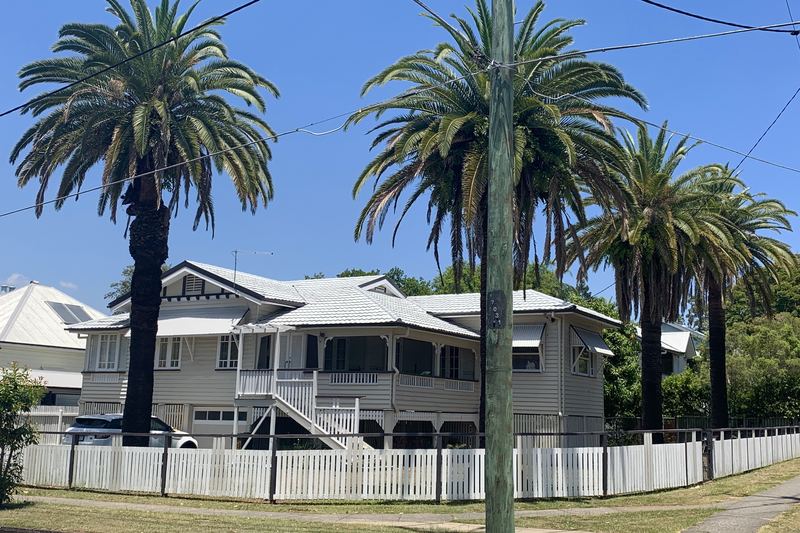 Queenslander house behind a picket fence and tall palms in Corinda, Brisbane